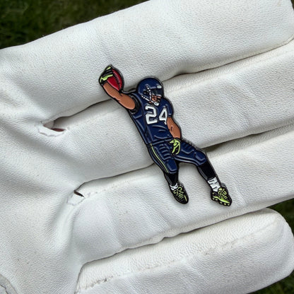 A small enamel pin shaped like an American football player in a navy blue uniform with the number 24, resting on a white leather golf glove.